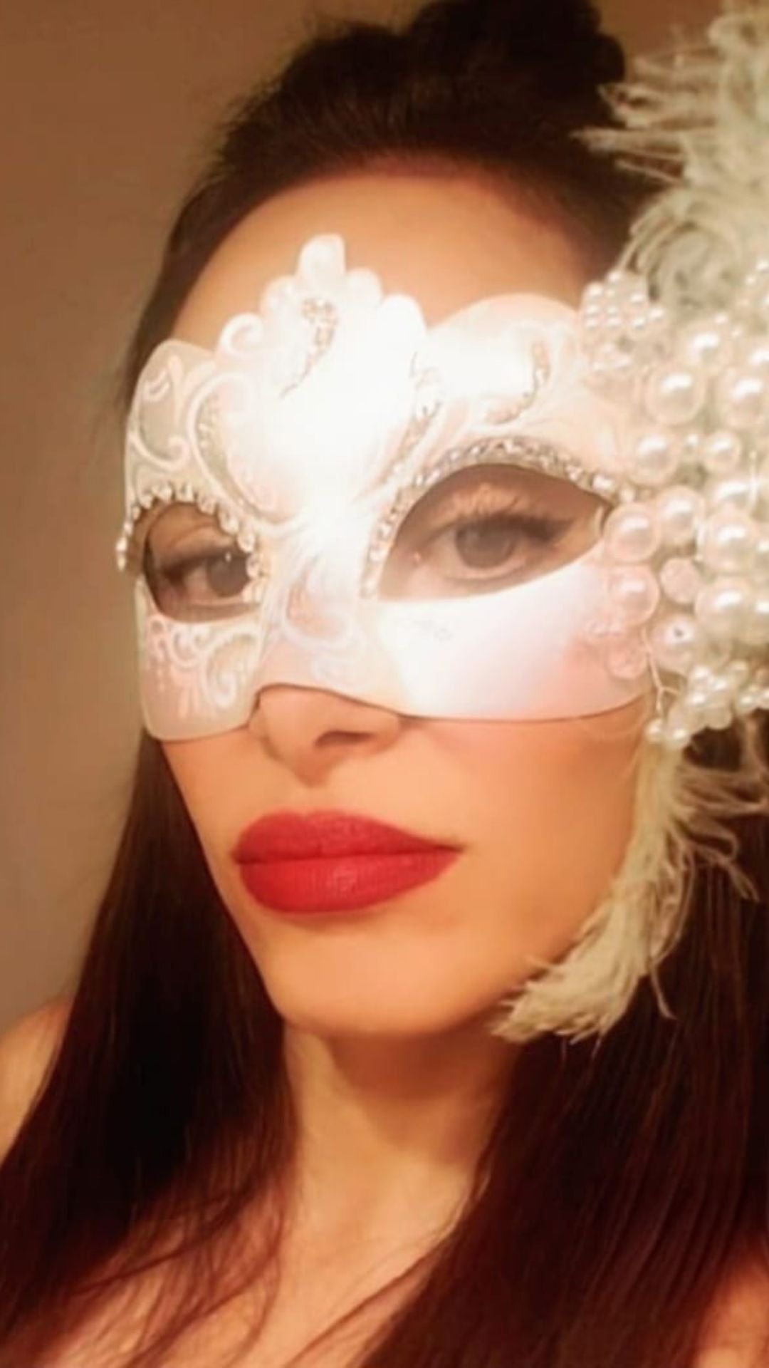 Yael James wearing an ornate white masquerade mask with pearls and feathers.