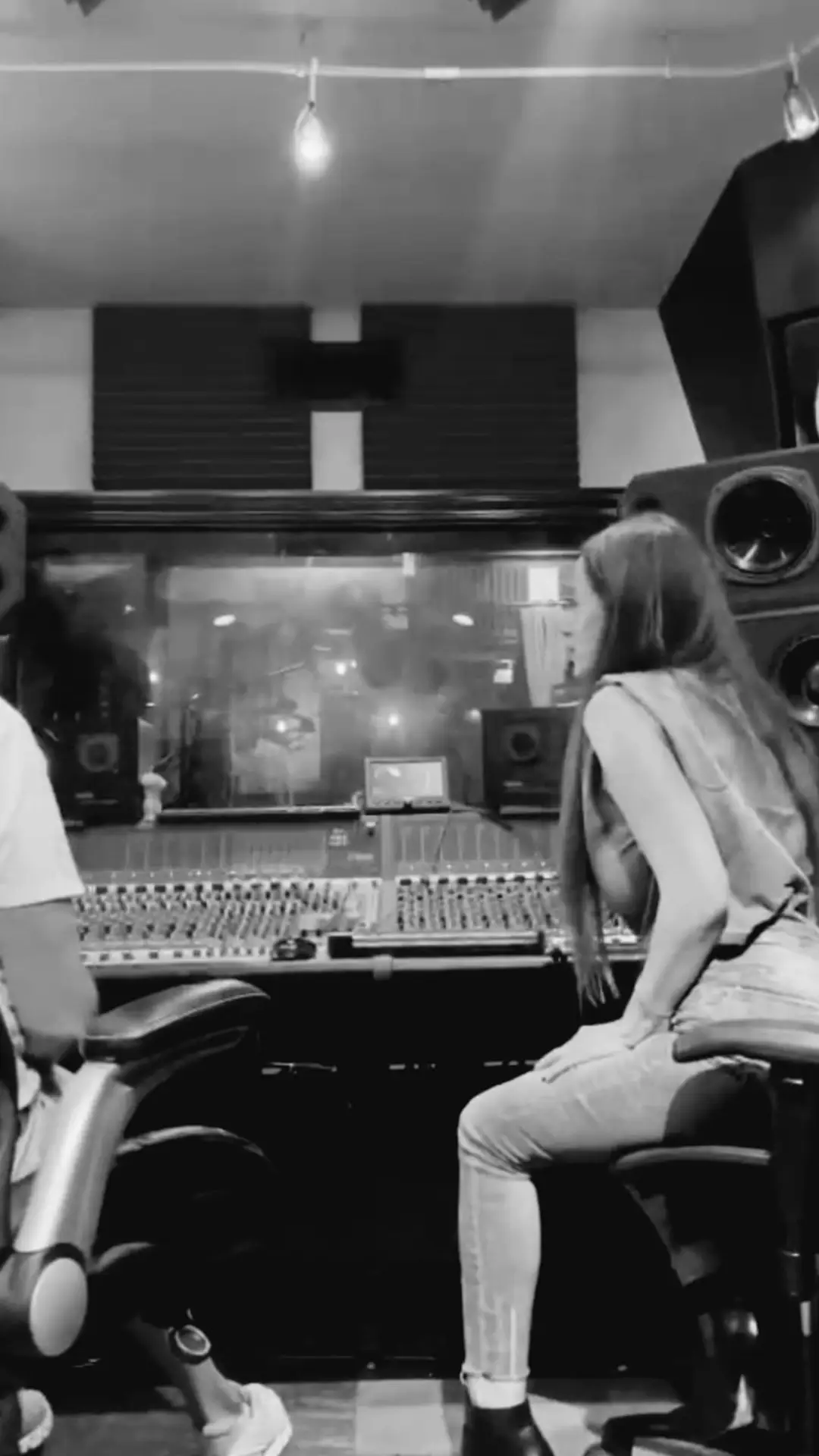 Black-and-white photo of a musician seated at a mixing console in a recording studio.